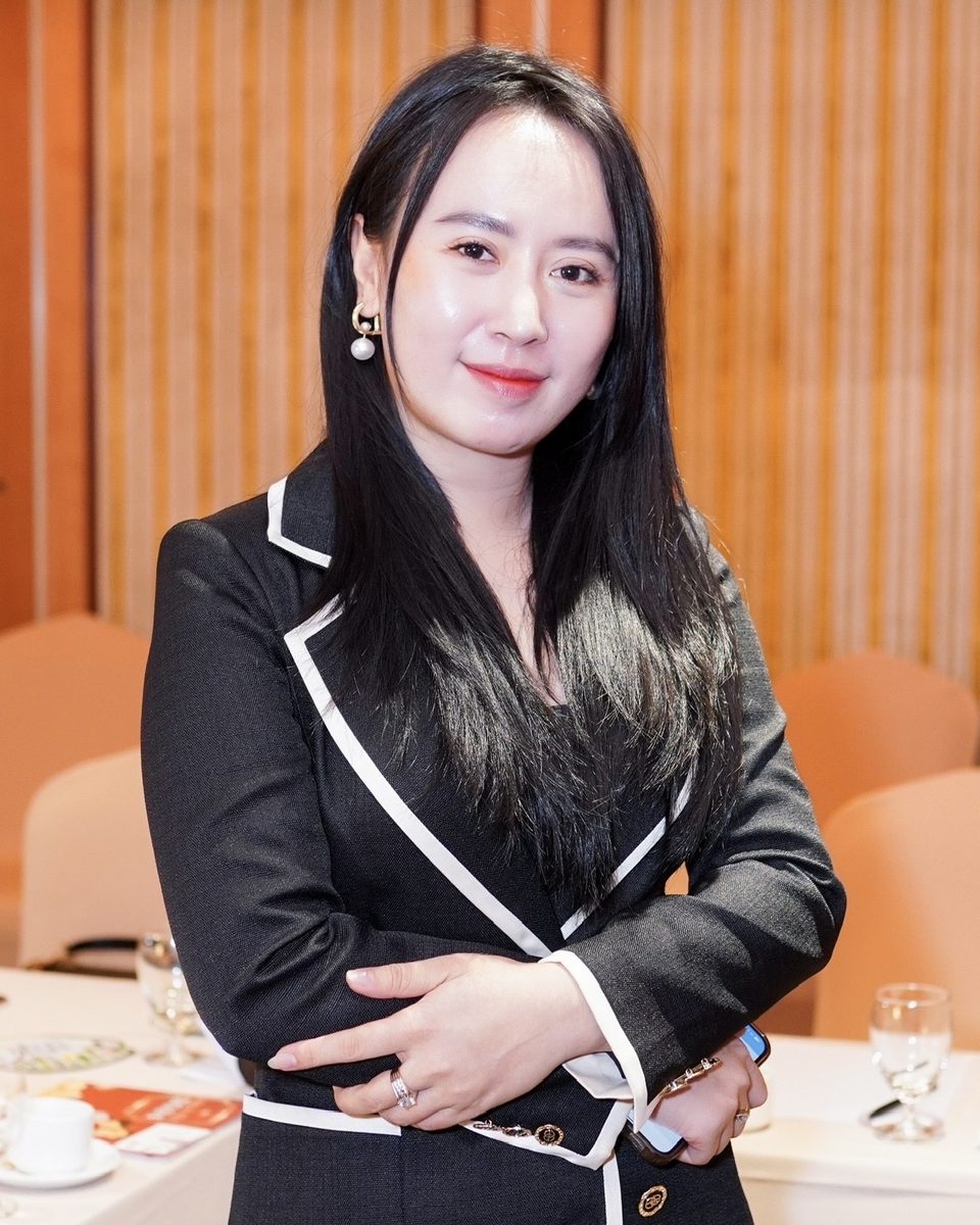 Nguyễn Lê Mỹ Huyền mặc vest đen, khoanh tay, đứng trong phòng hội thảo